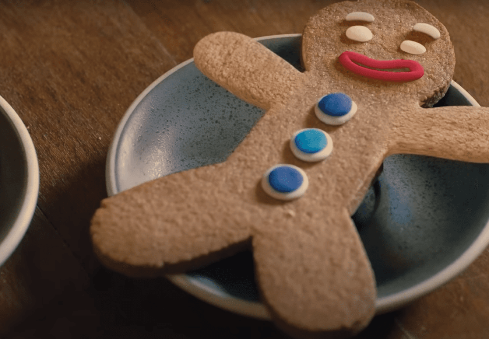 Gingerbread man cookie with blue buttons and a red smile on a blue ceramic plate.