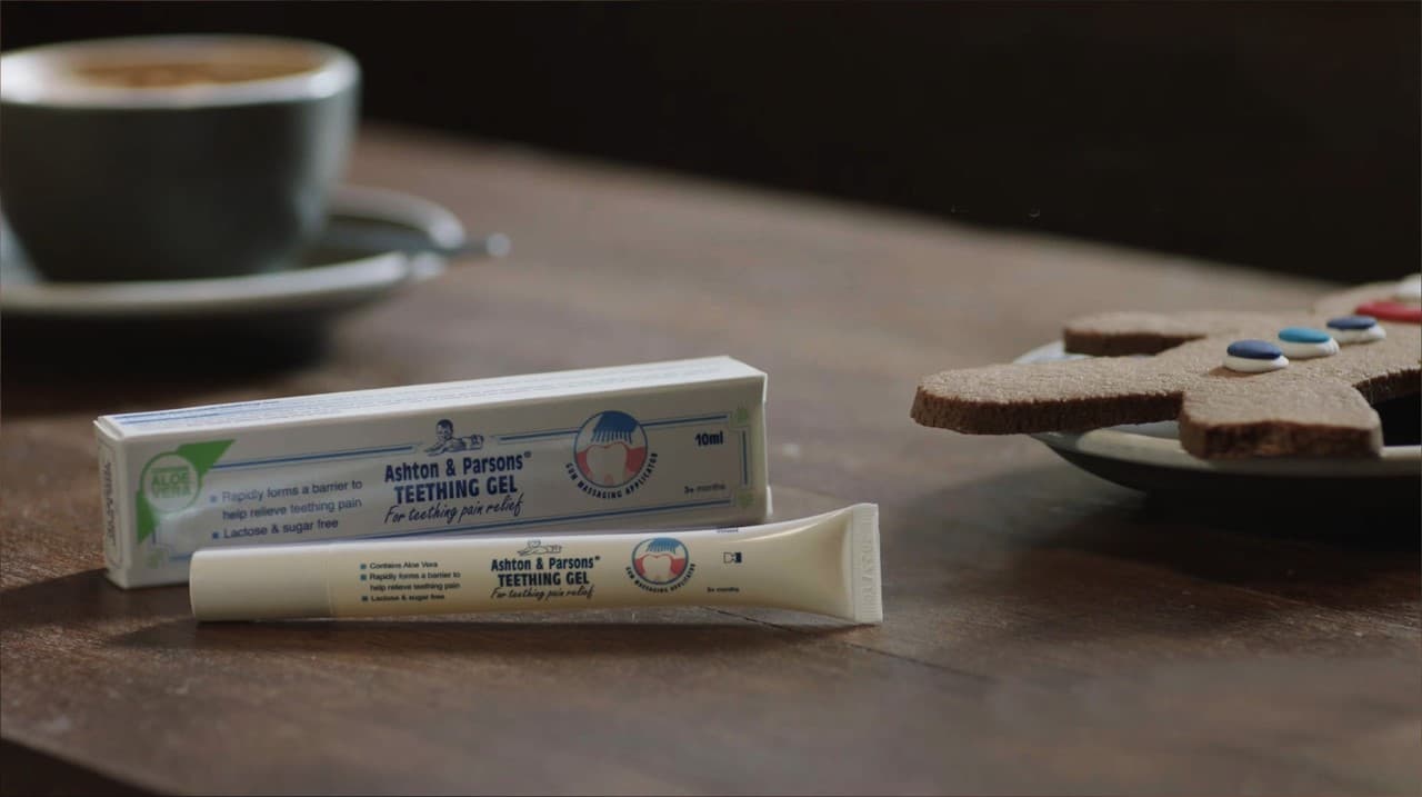 Ashton and Parsons Teething Gel packaging on a wooden table with coffee and a cookie.