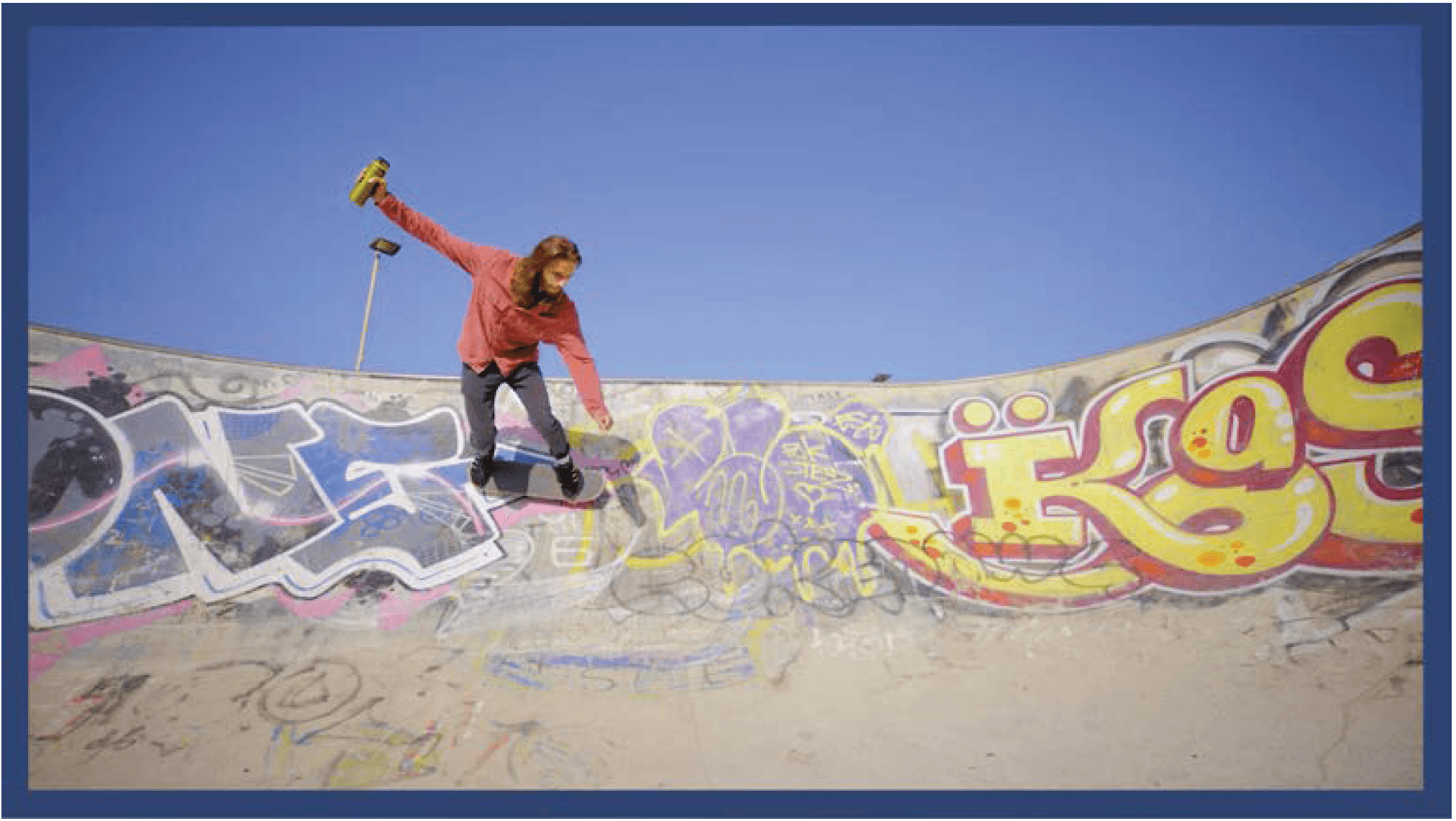 Skateboarder in a red shirt jumps over a graffiti ramp holding a green water bottle.
