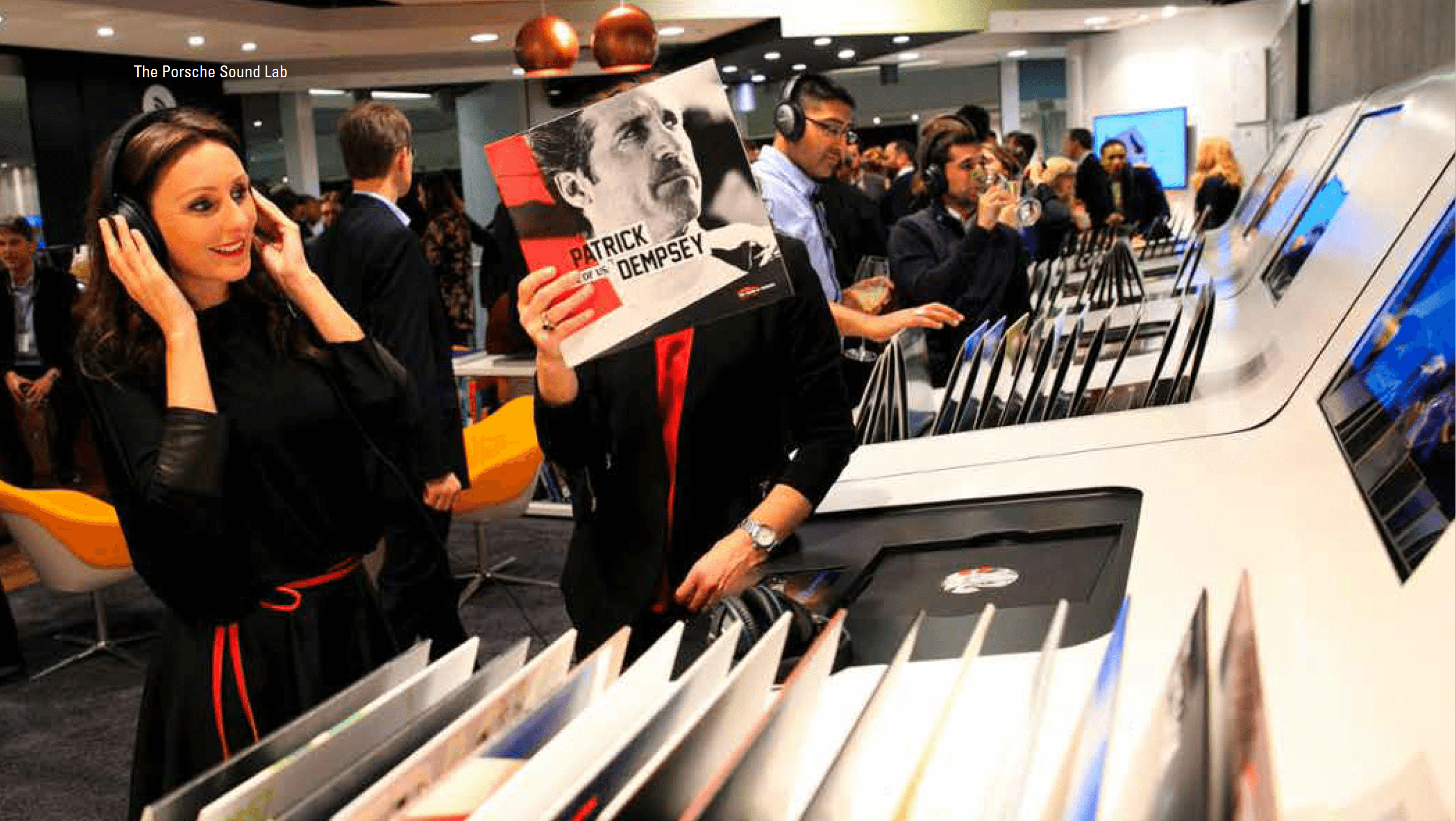 Guests wearing headphones and holding a Patrick Dempsey record at The Porsche Sound Lab.